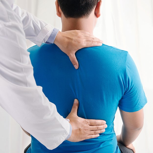 A doctor examining a patient’s back by placing hands on the upper and lower spine areas